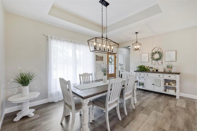 dining area with an inviting chandelier, light wood-type flooring, and a raised ceiling