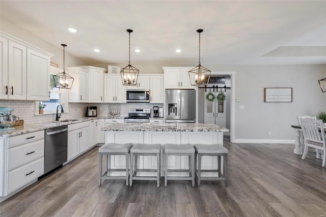 kitchen with appliances with stainless steel finishes, dark hardwood / wood-style flooring, light stone counters, and a kitchen island