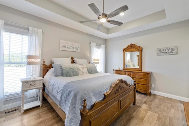 bedroom with light hardwood / wood-style flooring, ceiling fan, and a raised ceiling