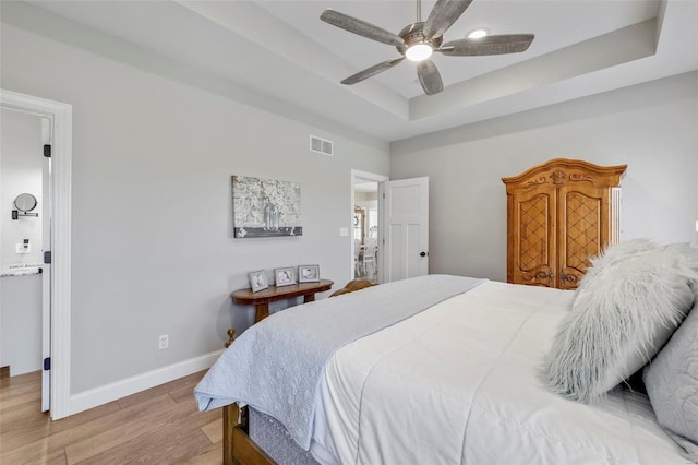 bedroom featuring ceiling fan, a raised ceiling, and light hardwood / wood-style floors