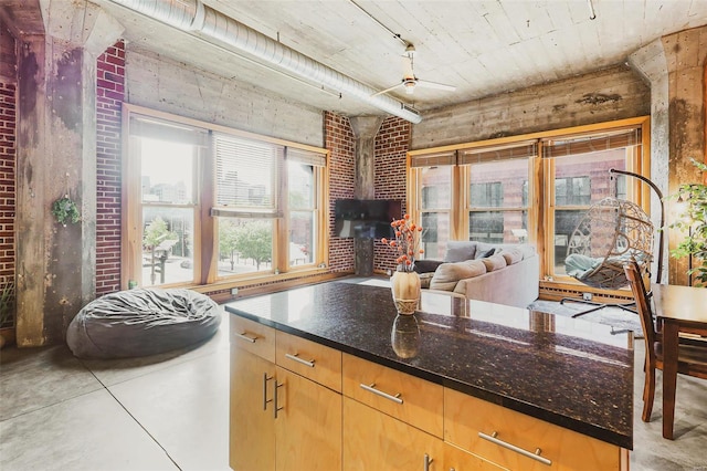 kitchen with a wood stove, ceiling fan, dark stone counters, and brick wall