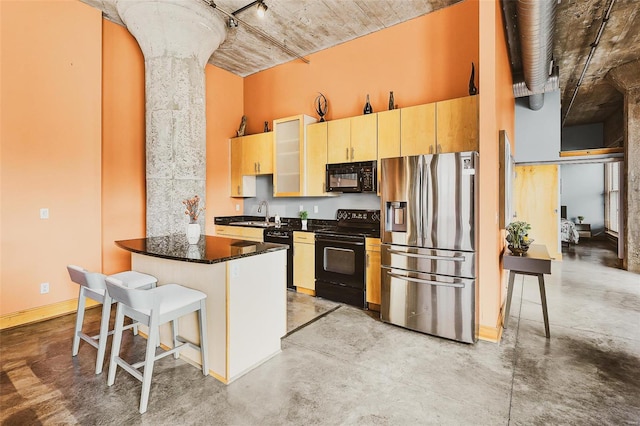 kitchen featuring a breakfast bar, decorative columns, kitchen peninsula, black appliances, and dark stone countertops