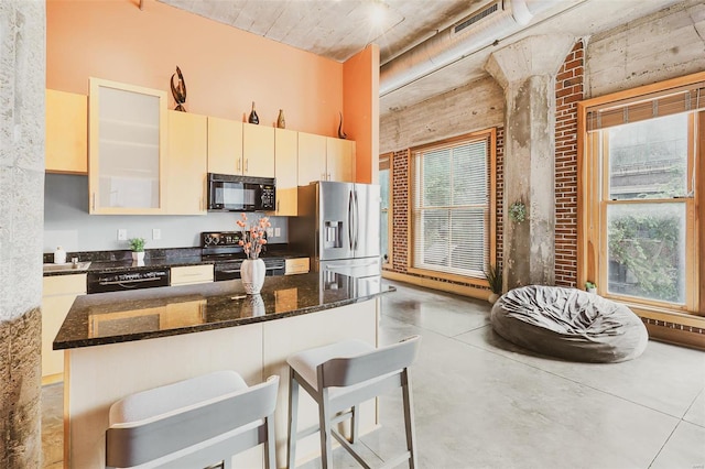 kitchen featuring electric stove, a breakfast bar area, dishwashing machine, stainless steel fridge, and dark stone countertops