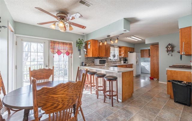 kitchen with light tile floors, kitchen peninsula, a textured ceiling, ceiling fan, and white appliances