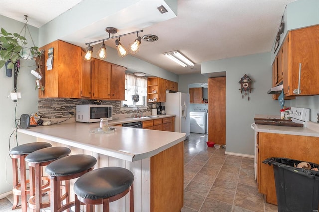 kitchen with a breakfast bar, white appliances, kitchen peninsula, washer / clothes dryer, and dark tile floors