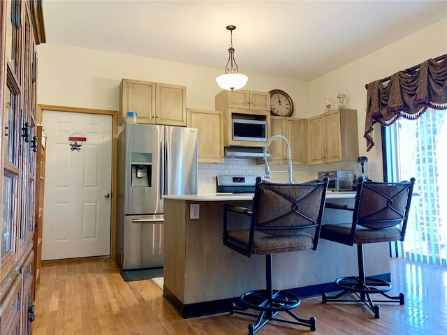 kitchen with hanging light fixtures, light hardwood / wood-style flooring, stainless steel appliances, tasteful backsplash, and light brown cabinetry