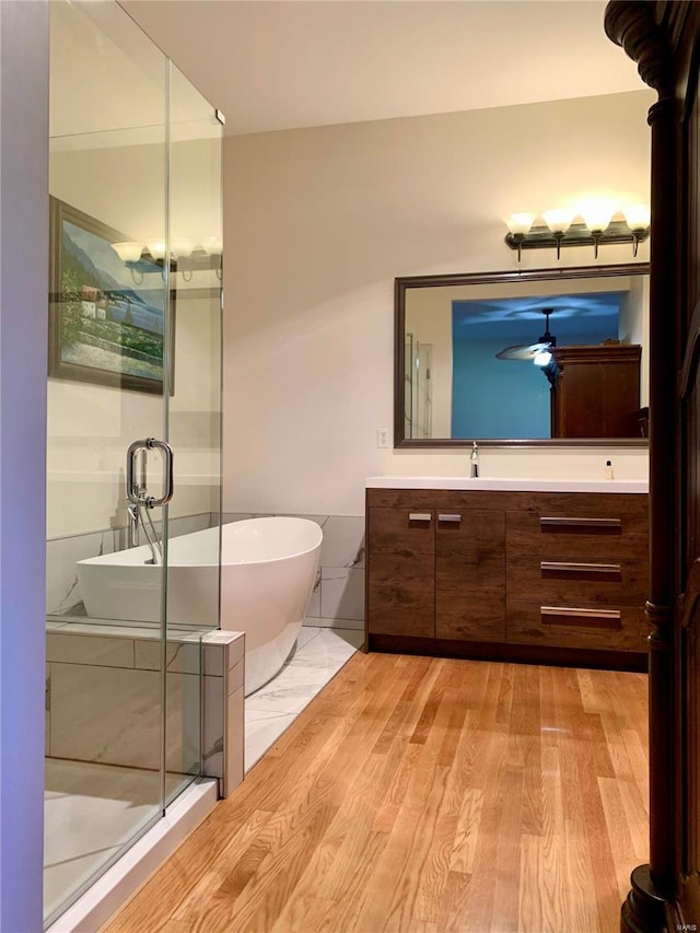 bathroom with independent shower and bath, a wood stove, ceiling fan, vanity, and hardwood / wood-style floors