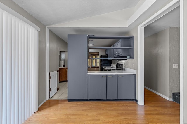 kitchen featuring backsplash, gray cabinetry, light hardwood / wood-style floors, and vaulted ceiling