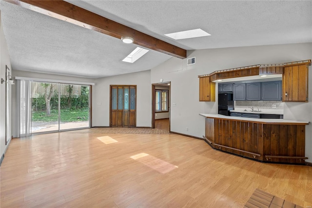 kitchen with lofted ceiling with skylight, sink, gray cabinets, light hardwood / wood-style flooring, and black fridge