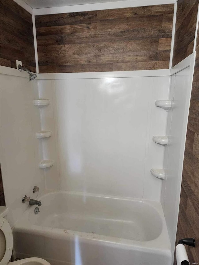 bathroom featuring washtub / shower combination, toilet, and wooden walls