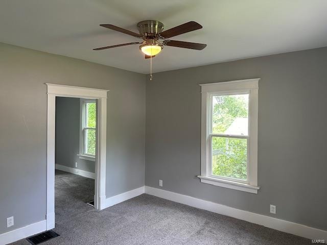 unfurnished room featuring a wealth of natural light, dark colored carpet, and ceiling fan