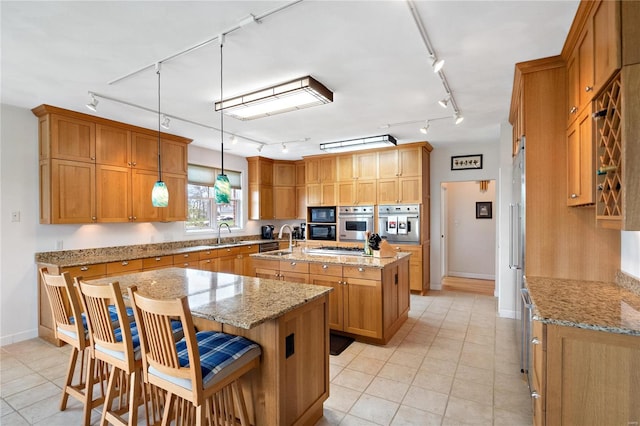 kitchen with a center island with sink, a breakfast bar area, track lighting, light stone countertops, and hanging light fixtures