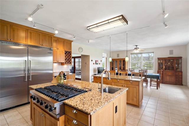 kitchen with appliances with stainless steel finishes, a center island with sink, light stone countertops, ceiling fan, and sink