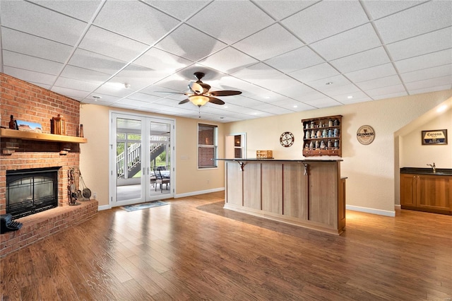 interior space with ceiling fan, a drop ceiling, hardwood / wood-style flooring, and a fireplace