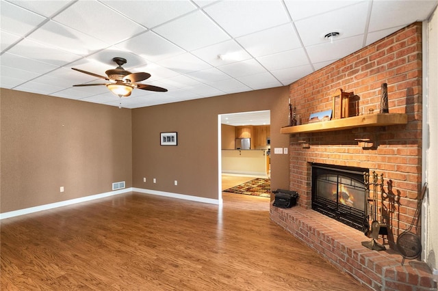 unfurnished living room with dark hardwood / wood-style flooring, a paneled ceiling, ceiling fan, and a brick fireplace