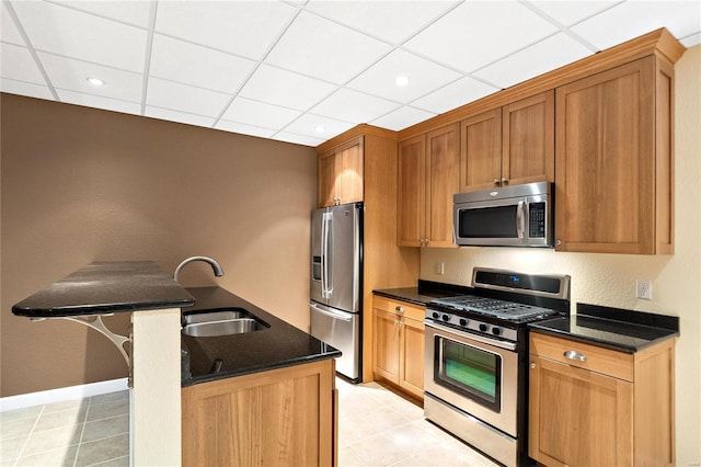 kitchen featuring a drop ceiling, appliances with stainless steel finishes, light tile floors, dark stone countertops, and sink