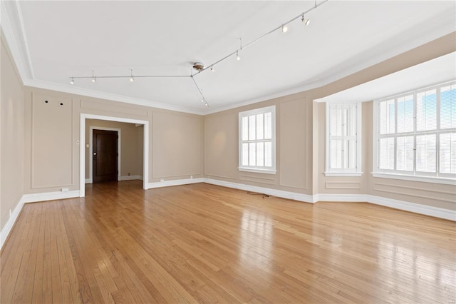 empty room with ornamental molding, track lighting, plenty of natural light, and light wood-type flooring