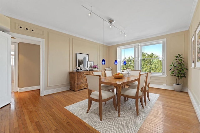 dining space with light hardwood / wood-style floors, ornamental molding, and rail lighting