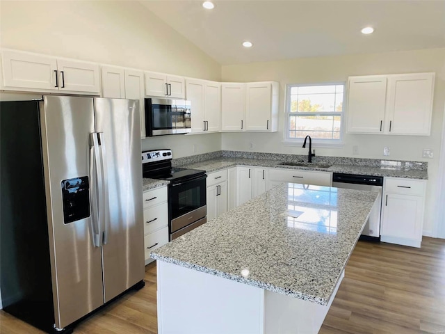 kitchen with a center island, white cabinets, stainless steel appliances, light hardwood / wood-style flooring, and light stone countertops