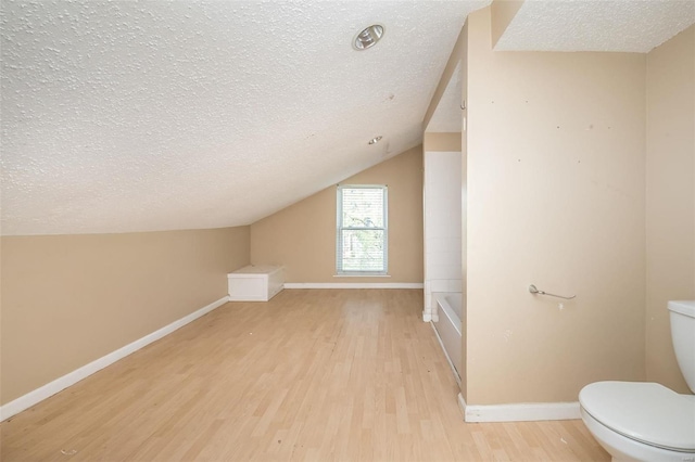 additional living space with light hardwood / wood-style flooring, vaulted ceiling, and a textured ceiling