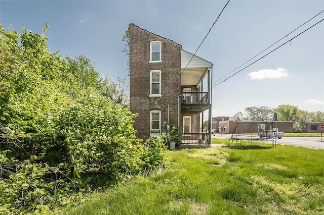 back of property with a yard, a trampoline, and a balcony