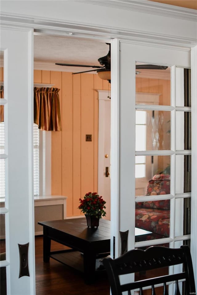 interior space with ceiling fan, radiator heating unit, ornamental molding, dark hardwood / wood-style flooring, and wood walls