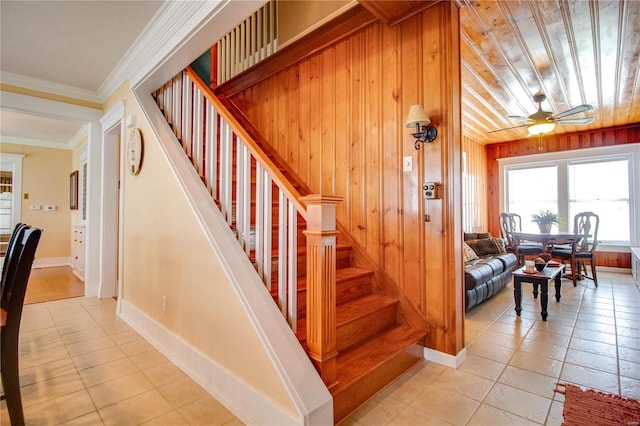 stairway with tile patterned flooring, crown molding, ceiling fan, and wood walls