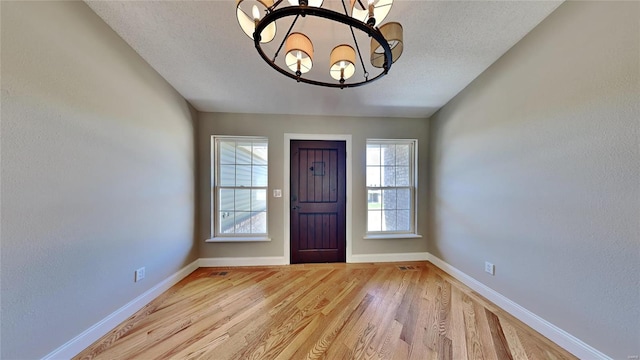 foyer entrance featuring a textured ceiling, a notable chandelier, and light hardwood / wood-style floors