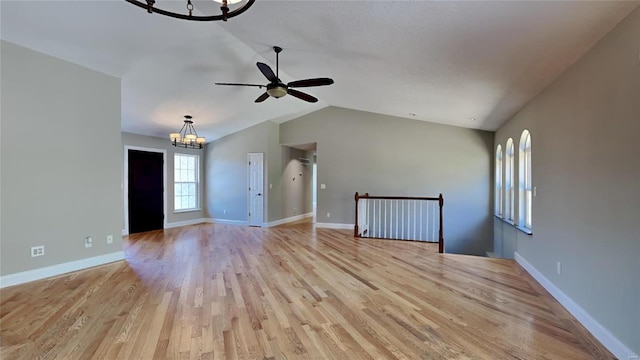 empty room featuring lofted ceiling, ceiling fan with notable chandelier, and light wood-type flooring