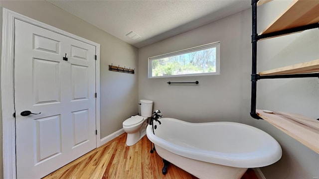 bathroom featuring a washtub, a textured ceiling, wood-type flooring, and toilet