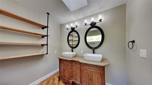 bathroom with a skylight, double sink vanity, hardwood / wood-style flooring, and a textured ceiling