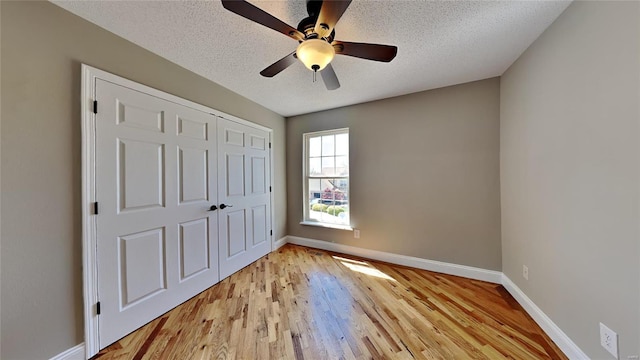 unfurnished bedroom featuring a closet, light hardwood / wood-style flooring, ceiling fan, and a textured ceiling