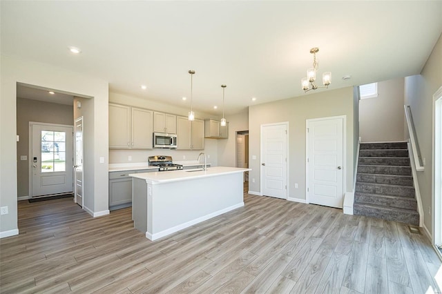 kitchen featuring gray cabinets, light hardwood / wood-style flooring, a kitchen island with sink, hanging light fixtures, and stainless steel appliances