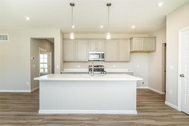 kitchen with pendant lighting, appliances with stainless steel finishes, light hardwood / wood-style floors, and a center island with sink