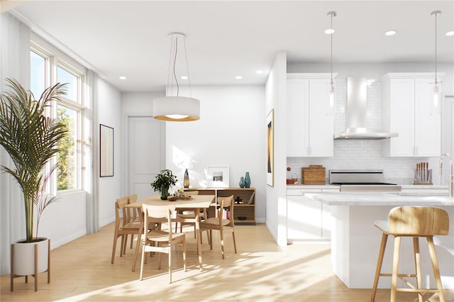 kitchen with hanging light fixtures, wall chimney range hood, white cabinets, and a healthy amount of sunlight