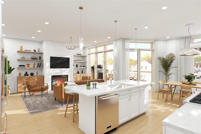 kitchen with pendant lighting, white cabinets, a tiled fireplace, sink, and dishwasher