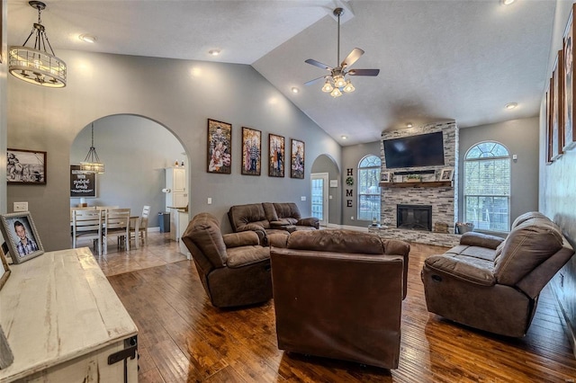 living room with high vaulted ceiling, ceiling fan, a stone fireplace, and dark hardwood / wood-style floors