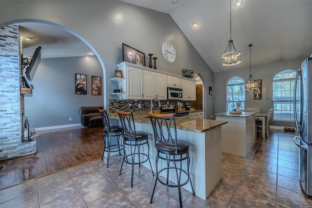 kitchen featuring appliances with stainless steel finishes, a kitchen island, tasteful backsplash, hanging light fixtures, and hardwood / wood-style flooring