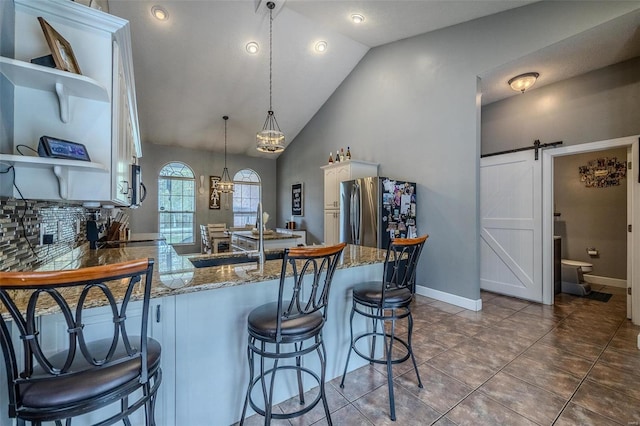 kitchen with a barn door, lofted ceiling, stainless steel refrigerator, white cabinets, and tile floors