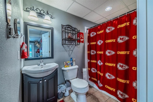 bathroom with tile flooring, a drop ceiling, vanity, and toilet