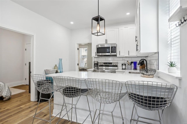 kitchen with decorative light fixtures, appliances with stainless steel finishes, kitchen peninsula, and white cabinetry