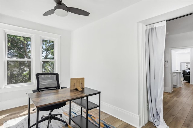 home office with light hardwood / wood-style floors and ceiling fan