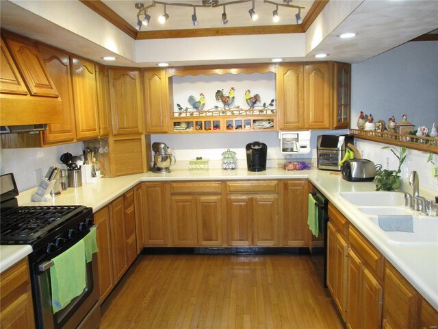 kitchen featuring black dishwasher, wood-type flooring, sink, gas range oven, and crown molding