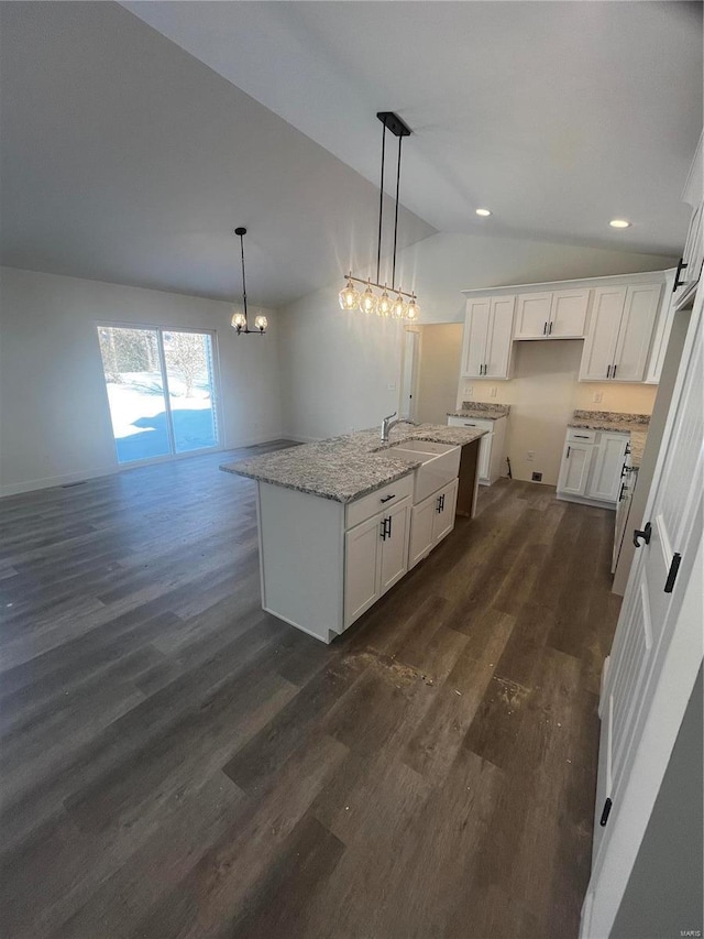 kitchen featuring white cabinets, vaulted ceiling, an island with sink, and light stone countertops