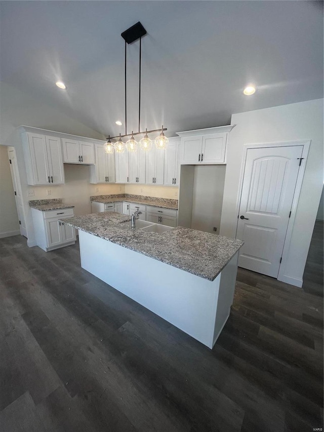 kitchen featuring a center island with sink, light stone countertops, white cabinets, decorative light fixtures, and lofted ceiling