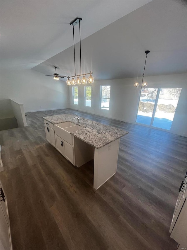 kitchen with light stone counters, pendant lighting, a kitchen island with sink, white cabinetry, and sink