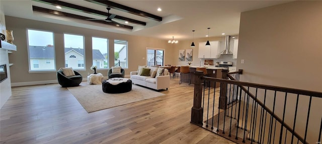 living room featuring beamed ceiling, ceiling fan with notable chandelier, and light hardwood / wood-style flooring