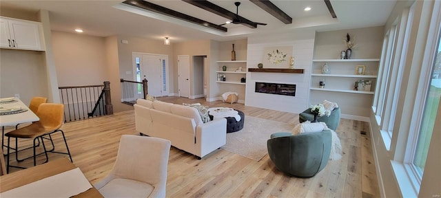 living room with built in shelves, ceiling fan, light wood-type flooring, and beam ceiling