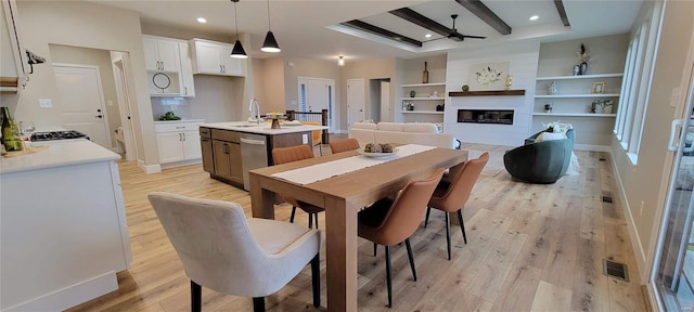 dining area featuring sink, built in shelves, ceiling fan, light wood-type flooring, and a fireplace