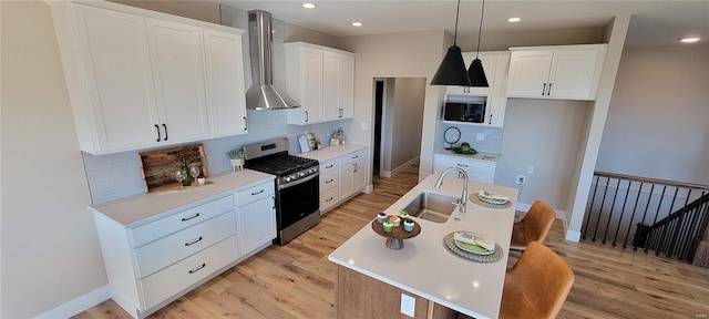 kitchen featuring a kitchen island with sink, white cabinets, sink, wall chimney exhaust hood, and stainless steel gas stove